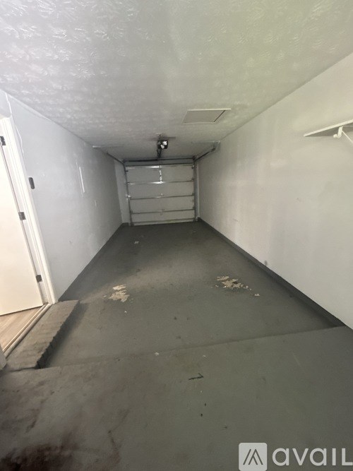 A long, narrow, unfinished room with a white door on the left and a white wall on the right.