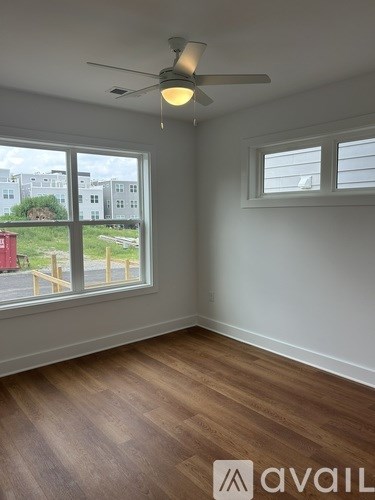 A room with a ceiling fan and a window overlooking a building.