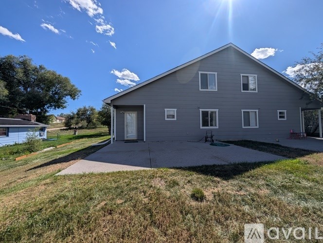 A house with a grey exterior and a white door is surrounded by a grassy area.
