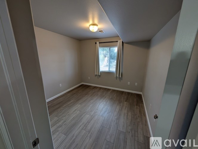 A room with wooden flooring and a window with a view of trees outside.