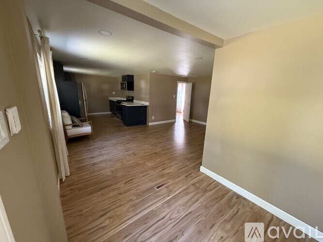 A spacious living room with wooden flooring and a kitchen area in the background.