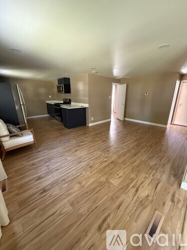 A spacious room with wooden flooring and a kitchen area in the background.