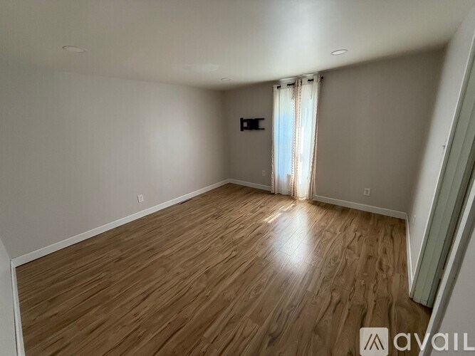 A room with wooden flooring and a window with curtains.