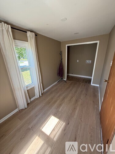 A room with wooden flooring and a window with curtains.