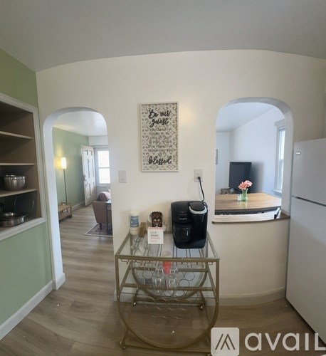 A kitchen with a white fridge, a table with a glass and a bottle on it, and a painting on the wall.