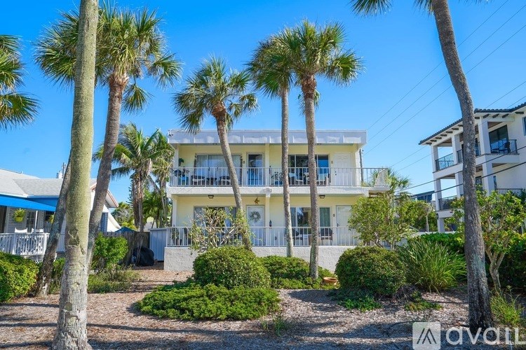 A row of palm trees in front of a white building with a balcony.