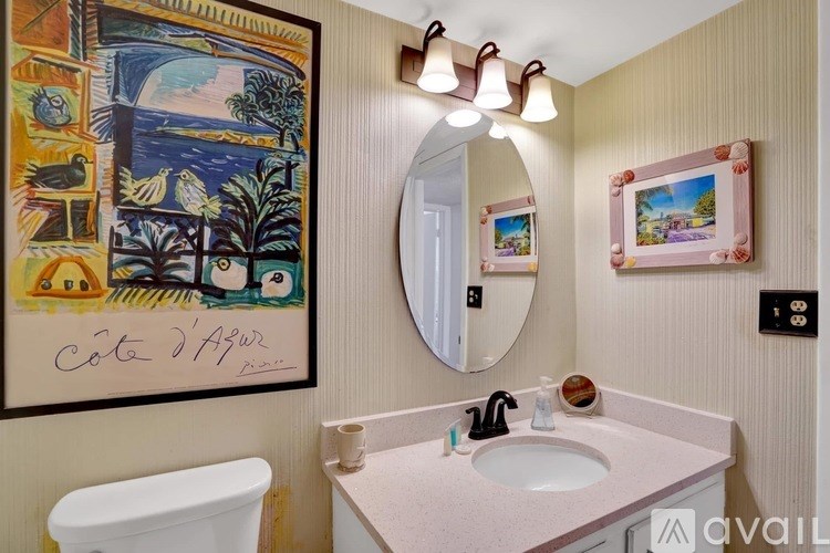 A bathroom with a painting on the wall and a mirror above the sink.