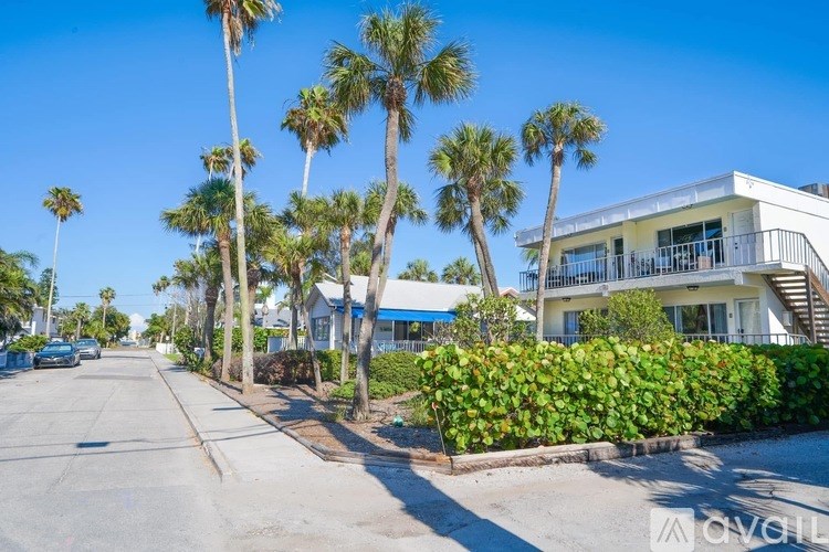 A street lined with palm trees and a white building on the right.