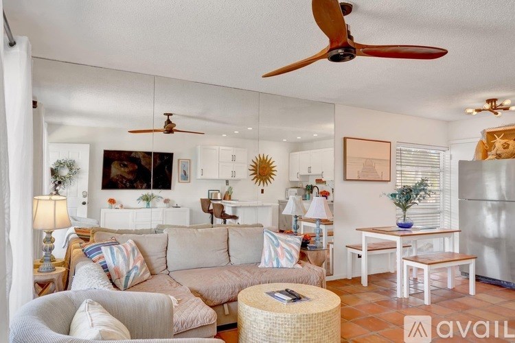 A living room with a couch, a fan, and a painting on the wall.