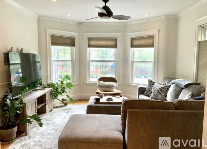 A living room with a brown couch, a television, and a ceiling fan.
