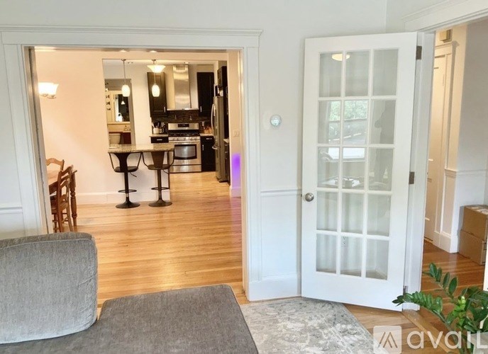 A living room with a grey couch and a glass door leading to a kitchen.