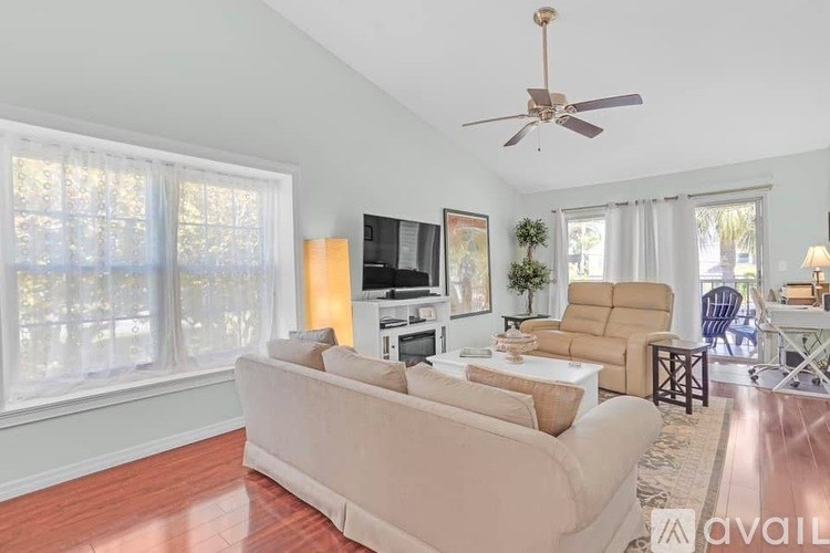 A living room with a beige couch, a ceiling fan, and a flat screen TV.