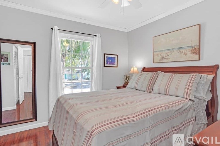 A bedroom with a bed, a painting, and a window with curtains.