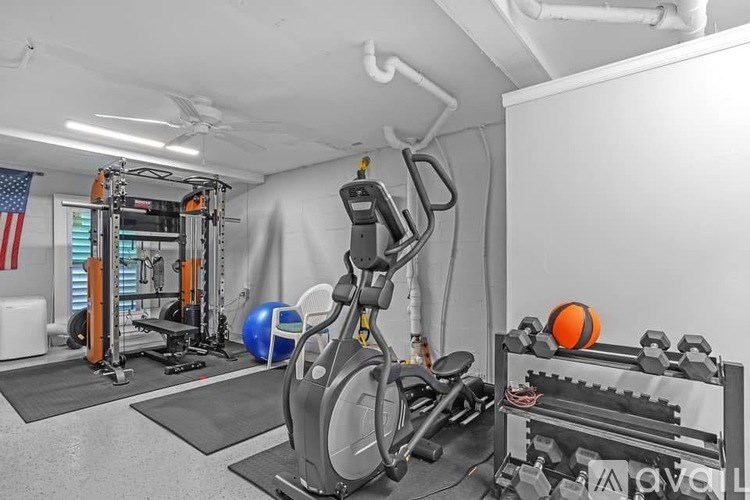A gym with a variety of equipment including a stationary bike, a weight bench, and a rowing machine.