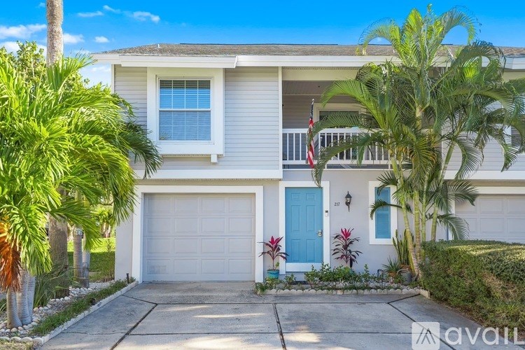A house with a blue door and a garage door is surrounded by greenery.