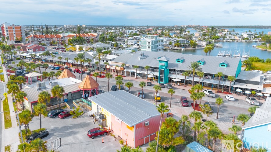 A view of a parking lot with a red car in the foreground and a building with a blue roof in the background.