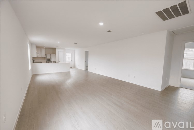 A spacious empty room with wooden flooring and white walls.