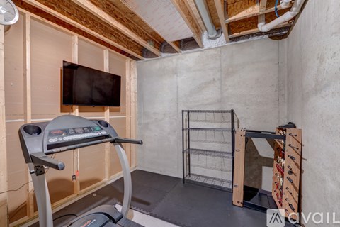 A treadmill is in a room under construction with a TV mounted on the wall.