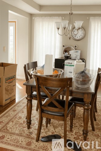 A dining room with a wooden table and chairs, a cardboard box, and a clock on the wall.