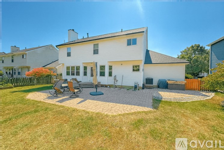 A house with a white exterior and a grey roof is surrounded by a fence and has a patio area with chairs and a table.