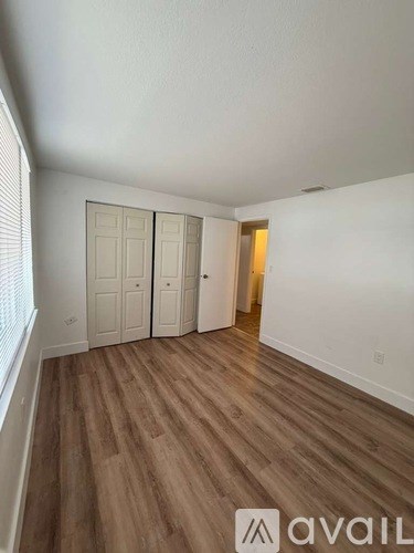 A room with wooden flooring and white walls, with a window on the left side.