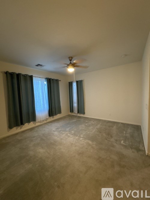 A room with a ceiling fan and two windows with curtains.