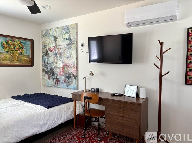 A bedroom with a bed, desk, chair, and a painting on the wall.