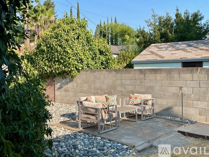 A patio with a couch and chairs is surrounded by a wall and a gravel area.
