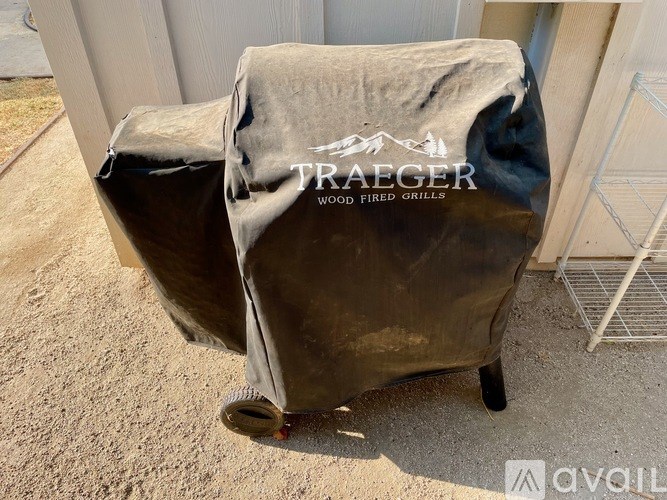 A grill is covered with a grey cloth that has the word "TRAEGER" on it.
