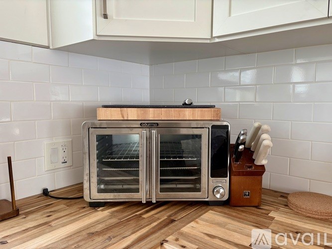 A toaster oven is placed on a wooden cutting board in a kitchen.