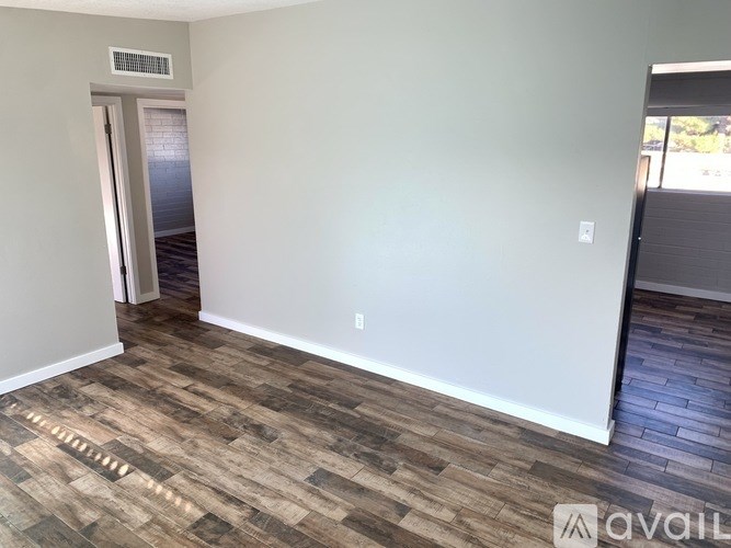 A room with a wooden floor and a white wall with a door leading to a balcony.