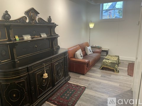 A living room with a black and gold chest of drawers, a brown leather sofa, and a small table with a lamp.