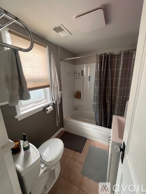 A white toilet sits in a bathroom with a shower curtain and a towel hanging on the window.