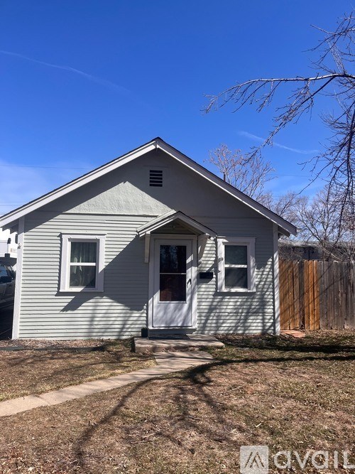 A small house with a white door and windows is surrounded by a fence.