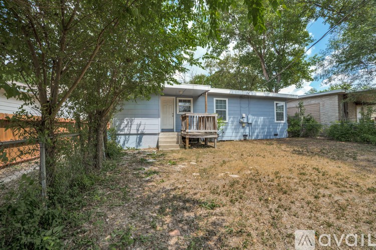 A house with a blue exterior is surrounded by trees and has a wooden deck.