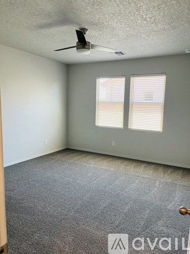 A room with a carpeted floor, a ceiling fan, and two windows with blinds.