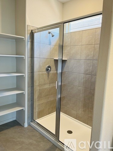 A shower area with a glass door and a white shelving unit.