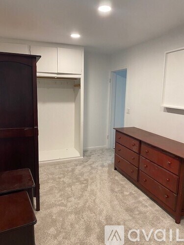 A room with a carpeted floor, a wooden dresser, and a wooden cabinet.