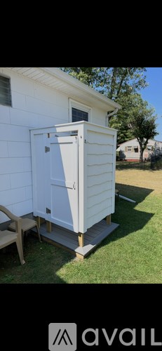 A white shed with a door open is situated in a grassy area.