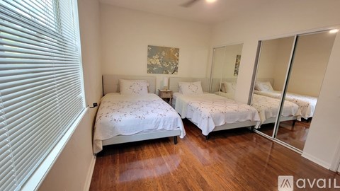 Two beds with white bedspreads and pillows in a room with wooden floors.