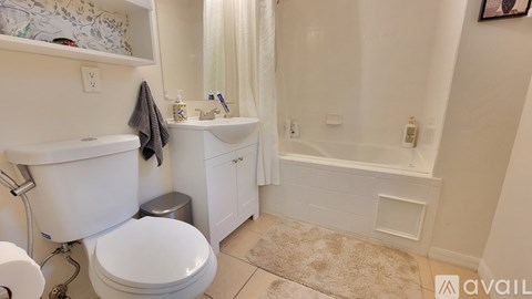 A white toilet with a towel hanging on the side of a white bathtub in a bathroom.