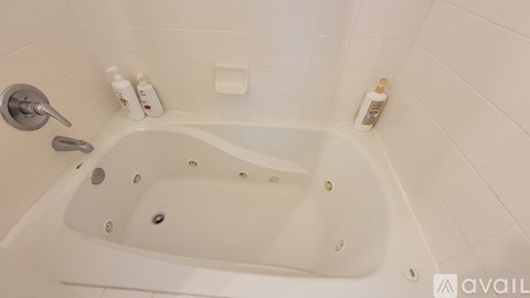 A white bathtub with a shower head and a bottle of lotion on the side.