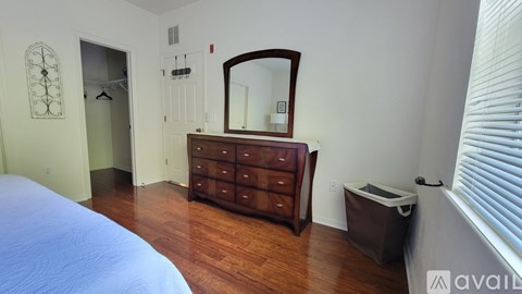 A bedroom with a bed, dresser, mirror, and trash can.
