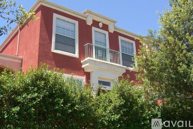 A red building with a balcony and windows surrounded by greenery.