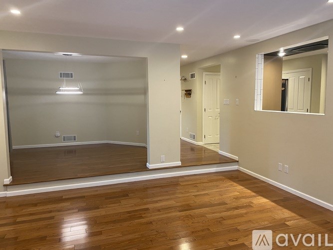 A spacious room with wooden floors and a large mirror on the wall.