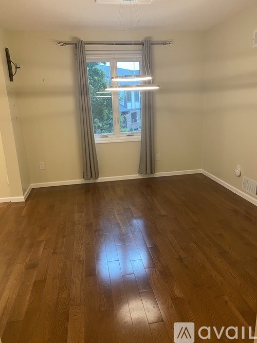 A room with wooden flooring and a window with curtains.