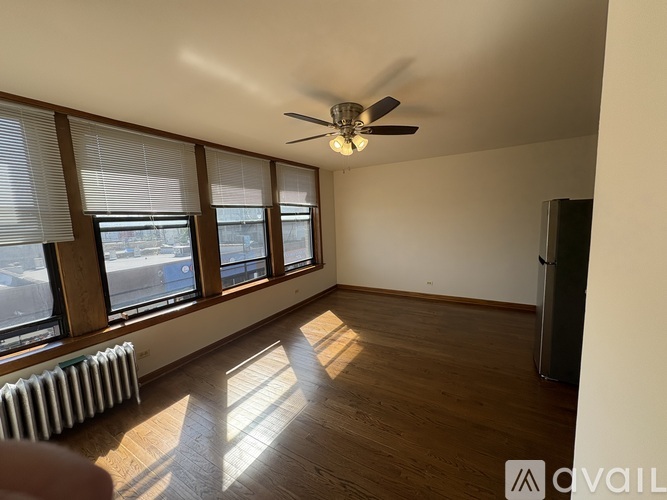 A room with a ceiling fan, wooden floors, and a window with blinds.
