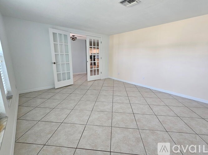 A room with white walls and tiled flooring, with a doorway leading to another room.