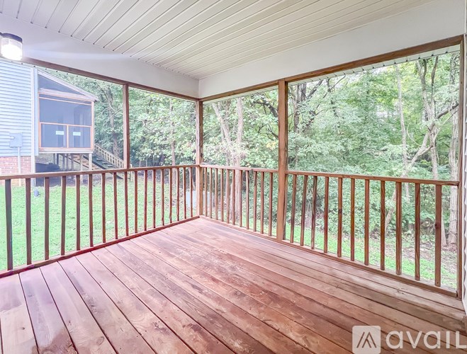 A wooden deck with a railing and a view of trees and a house.