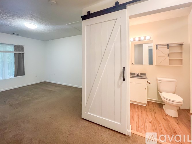 A white door is open to a bathroom with a toilet and a mirror.